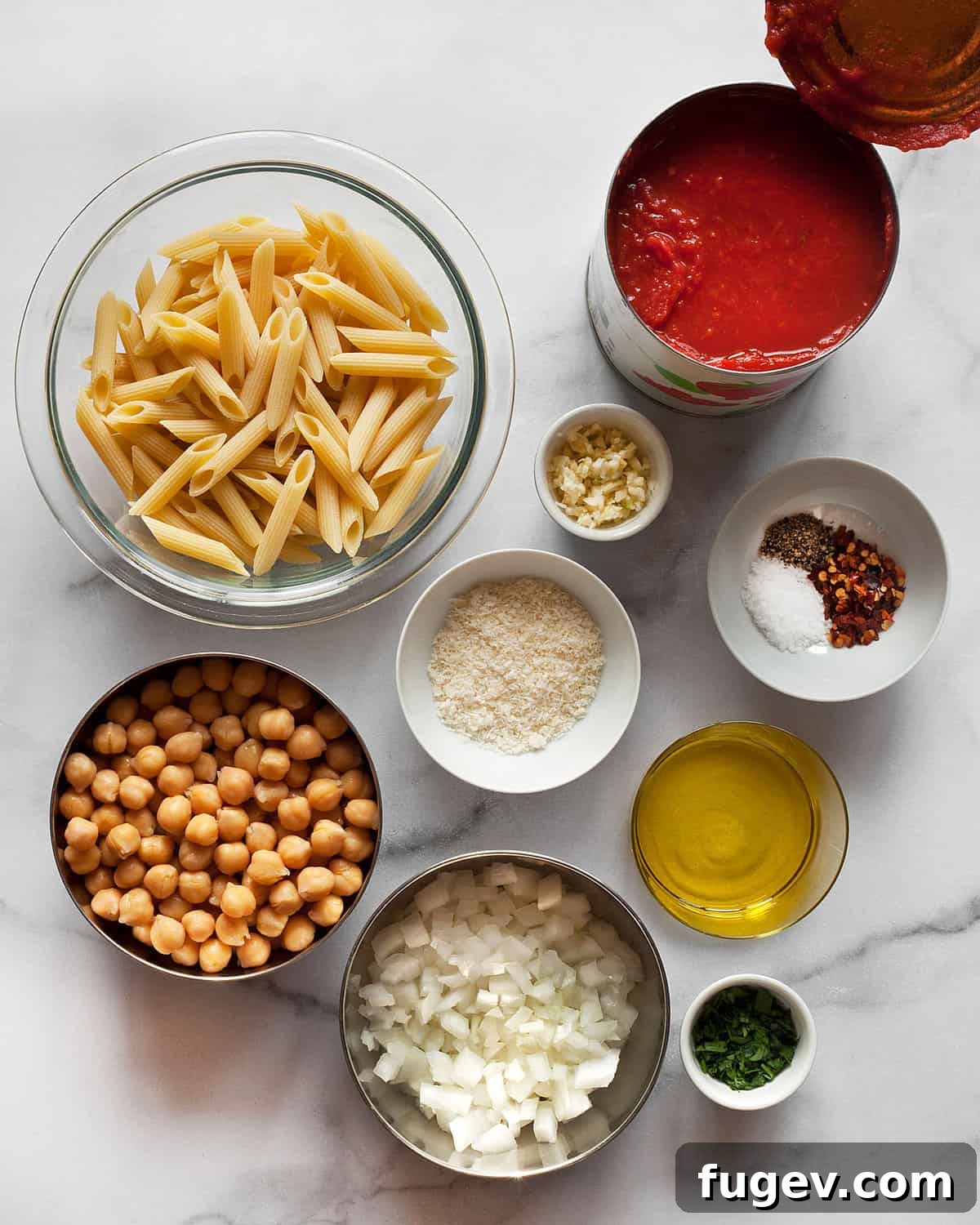 Arrabbiata Penne with a Chickpea Twist 3 A collection of fresh ingredients laid out on a table, including dry penne pasta, canned chickpeas, canned crushed tomatoes, garlic cloves, onions, red pepper flakes, olive oil, and fresh parsley, all ready for making Penne Arrabbiata.