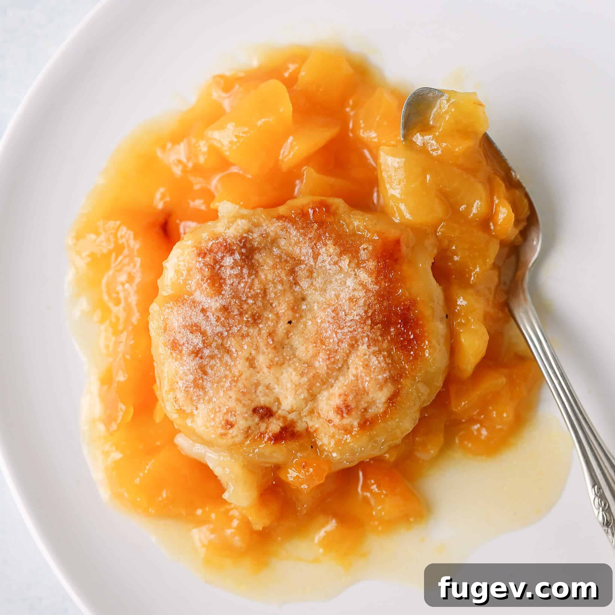 Southern Comfort Peach Cobbler 3 Old Fashioned Peach Cobbler on a white plate with a vintage spoon, ready to be enjoyed.