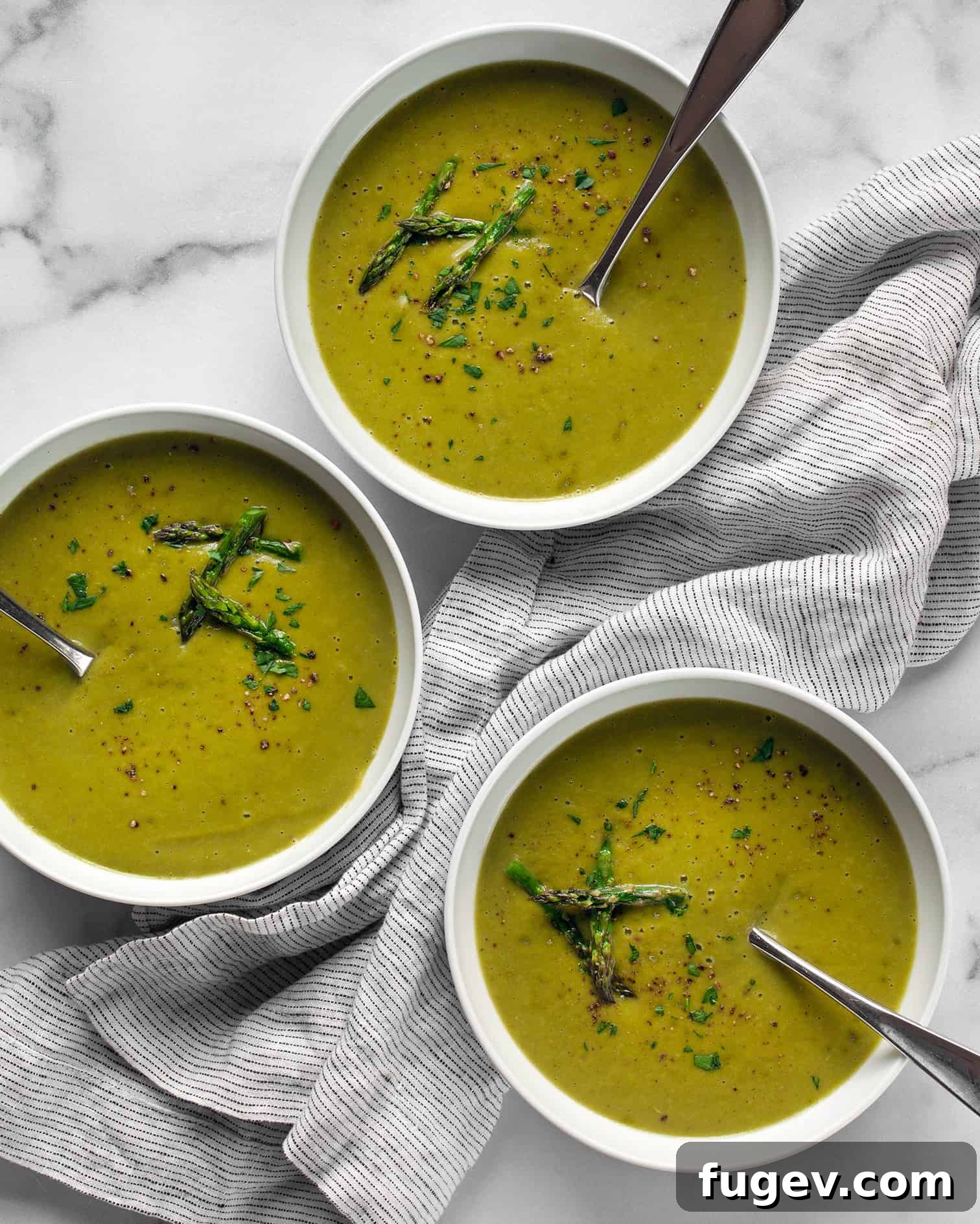 Silky Roasted Asparagus Soup 2 Three bowls of creamy roasted asparagus soup, garnished with fresh herbs.