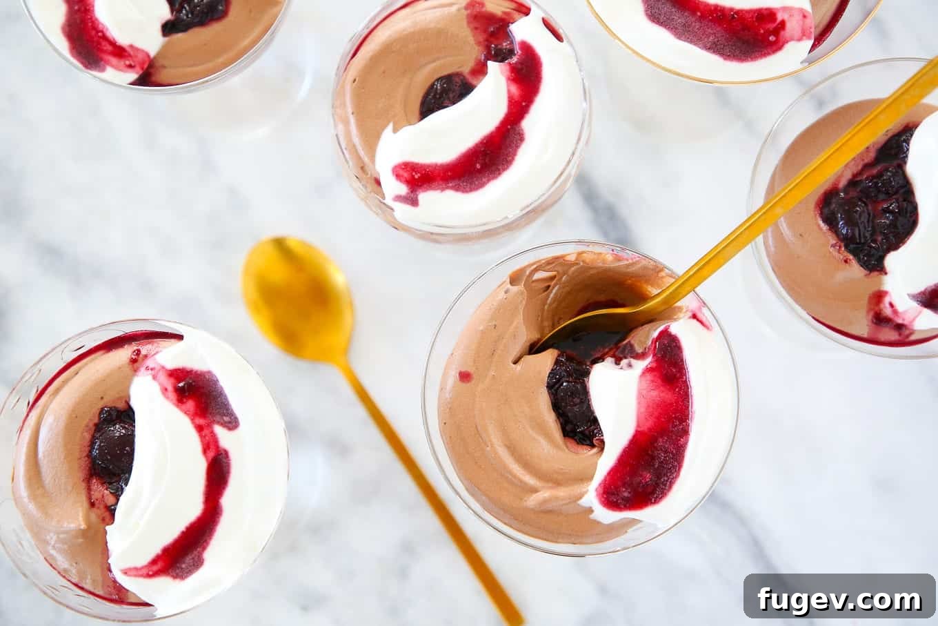 Velvet Chocolate Mousse 3 Two elegant glass coupes filled with smooth chocolate mousse and swirled cherry sauce, garnished with fresh cherries, set on a pristine white marble surface, highlighting the dessert's readiness for serving.