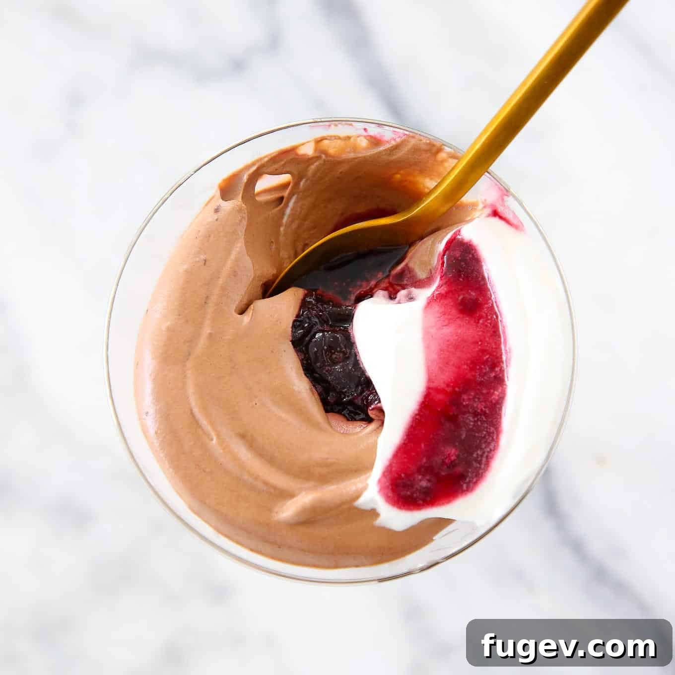 Velvet Chocolate Mousse 4 A trio of elegant glass coupes filled with homemade chocolate mousse, artfully swirled with ruby-red cherry sauce and crowned with fresh cherries, showcased on a minimalist white countertop.