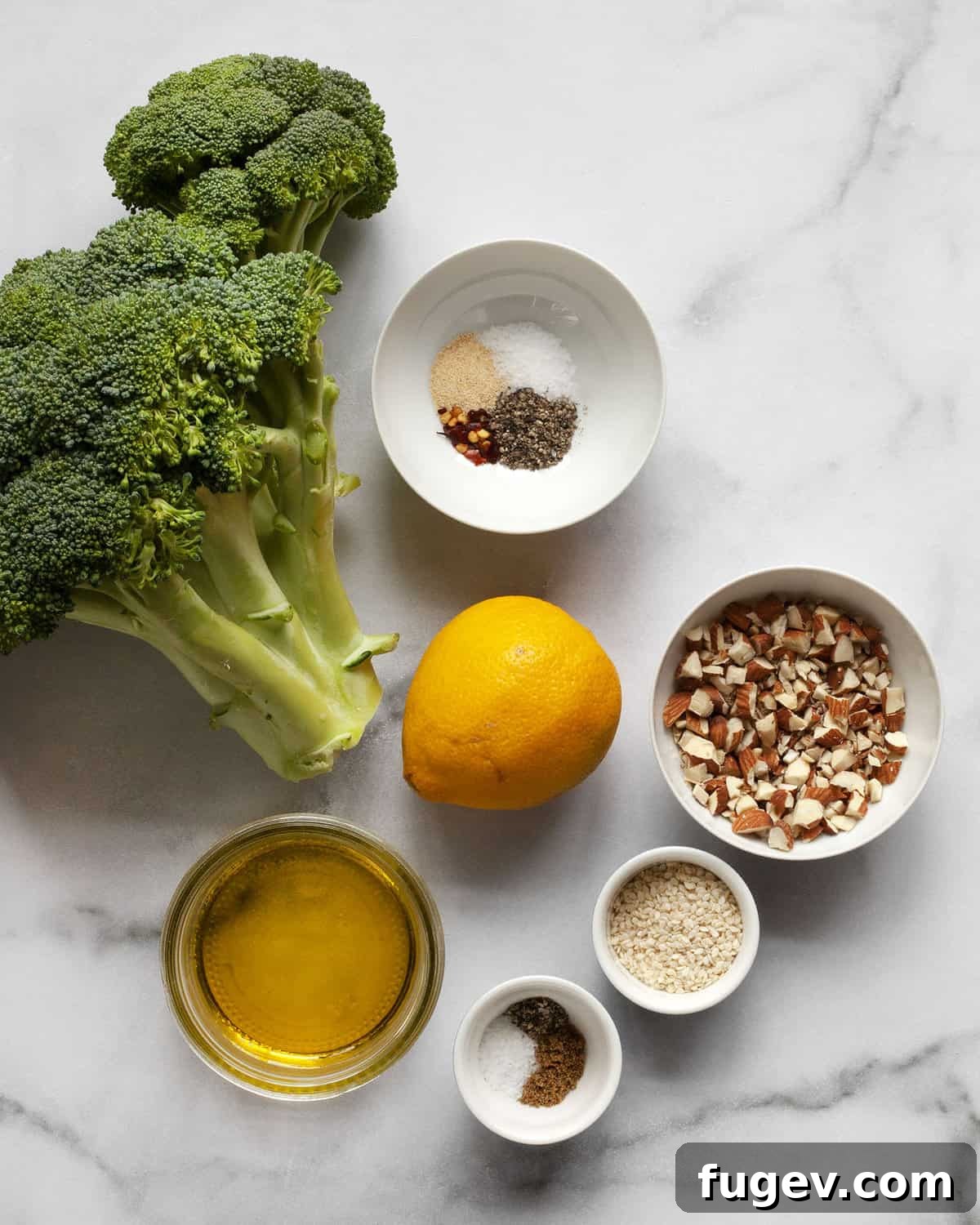 Smoky Lemon-Kissed Broccoli 3 Fresh ingredients laid out: broccoli, lemon, olive oil, almonds, sesame seeds, garlic powder, red pepper flakes, cumin, salt, and pepper.