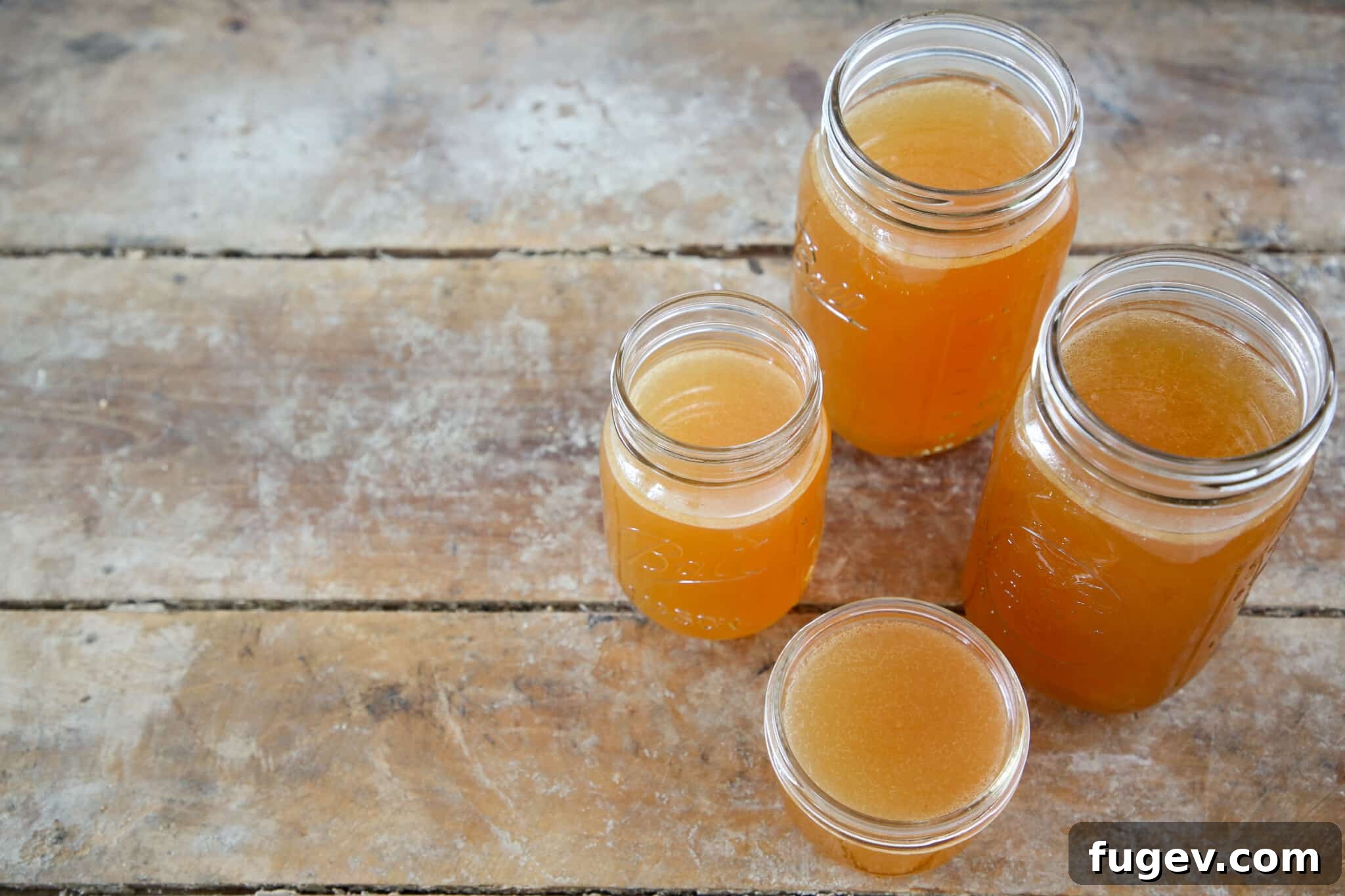 Mastering the Art of Golden Chicken Broth 3 Four jars of golden chicken stock beautifully arranged on a rustic wooden surface.