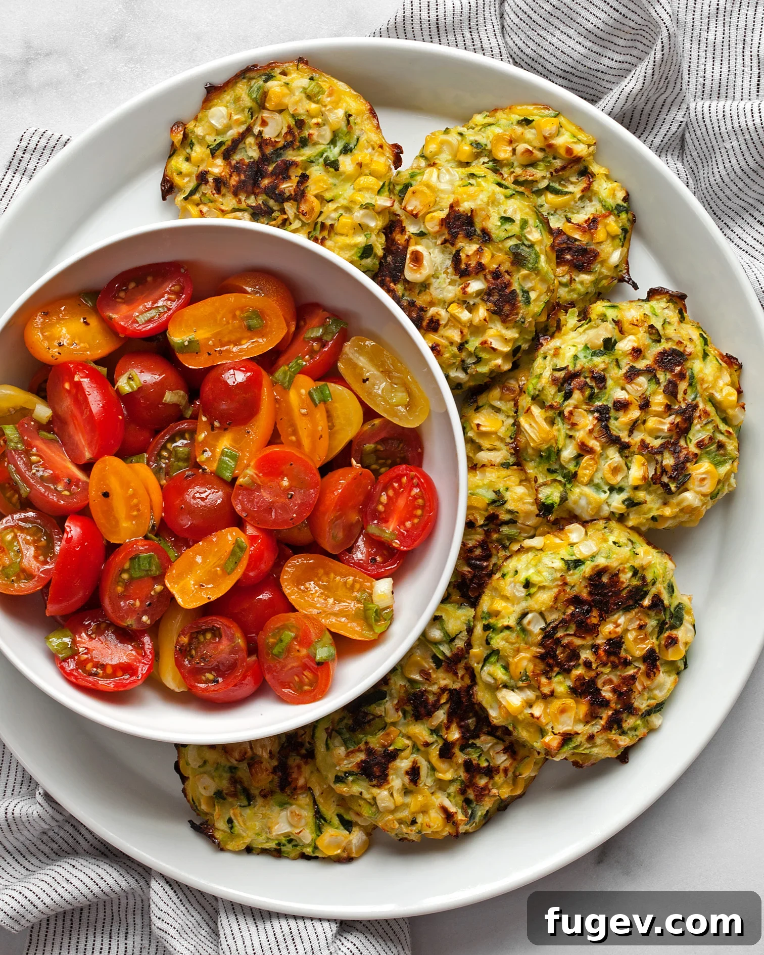 Golden Baked Zucchini Corn Fritters 2 Baked zucchini corn fritters on a plate with a tomato salad, highlighting their golden edges and fresh appeal.