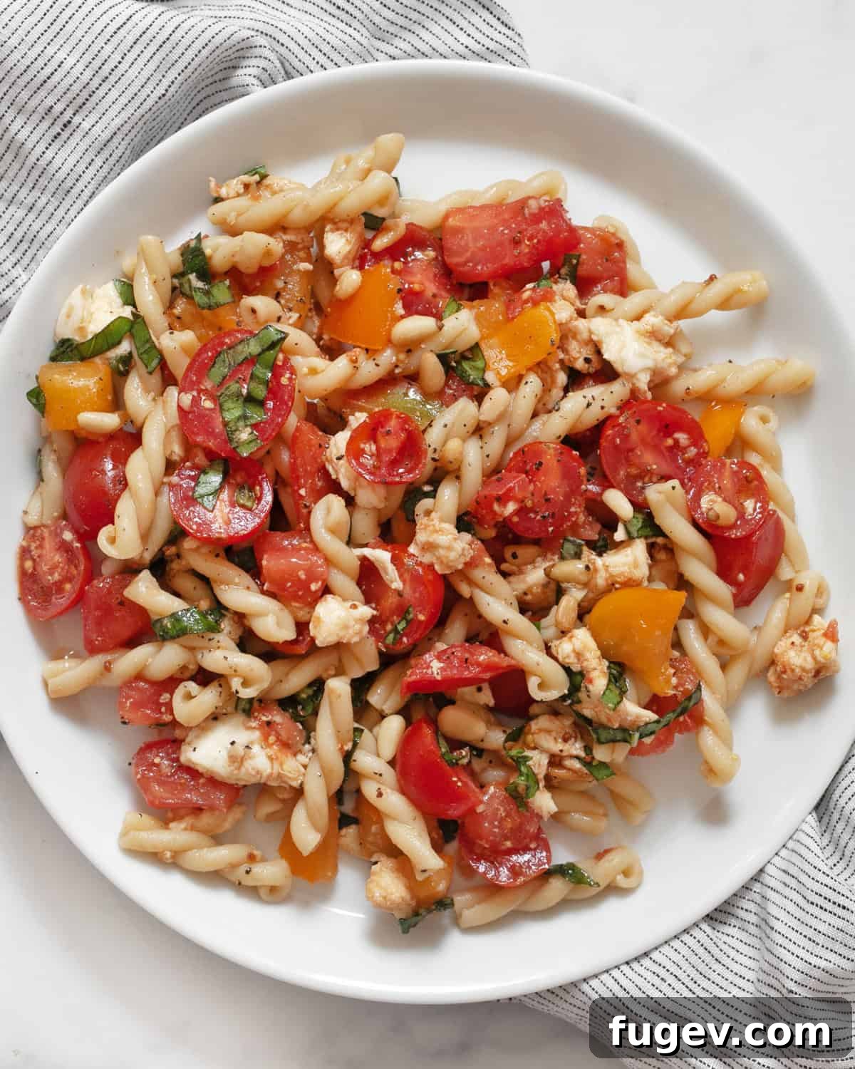 Bruschetta Inspired Pasta Salad 6 A beautifully arranged serving of Bruschetta Pasta Salad on a plate, garnished with fresh basil leaves.