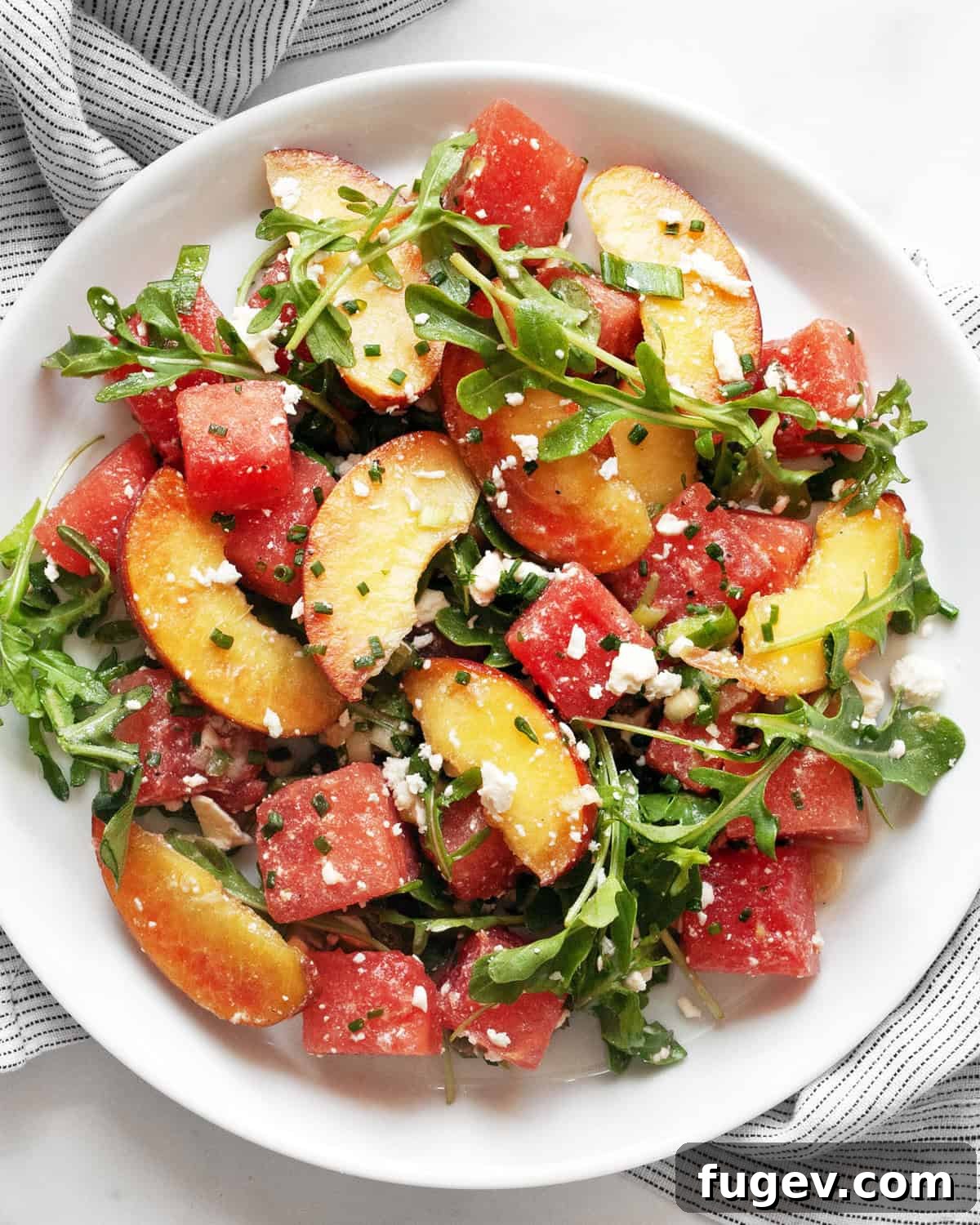 Watermelon Peach Bliss 2 A vibrant bowl of Watermelon Peach Salad, showcasing cubed watermelon, sliced peaches, crumbled feta, and fresh arugula, drizzled with dressing.