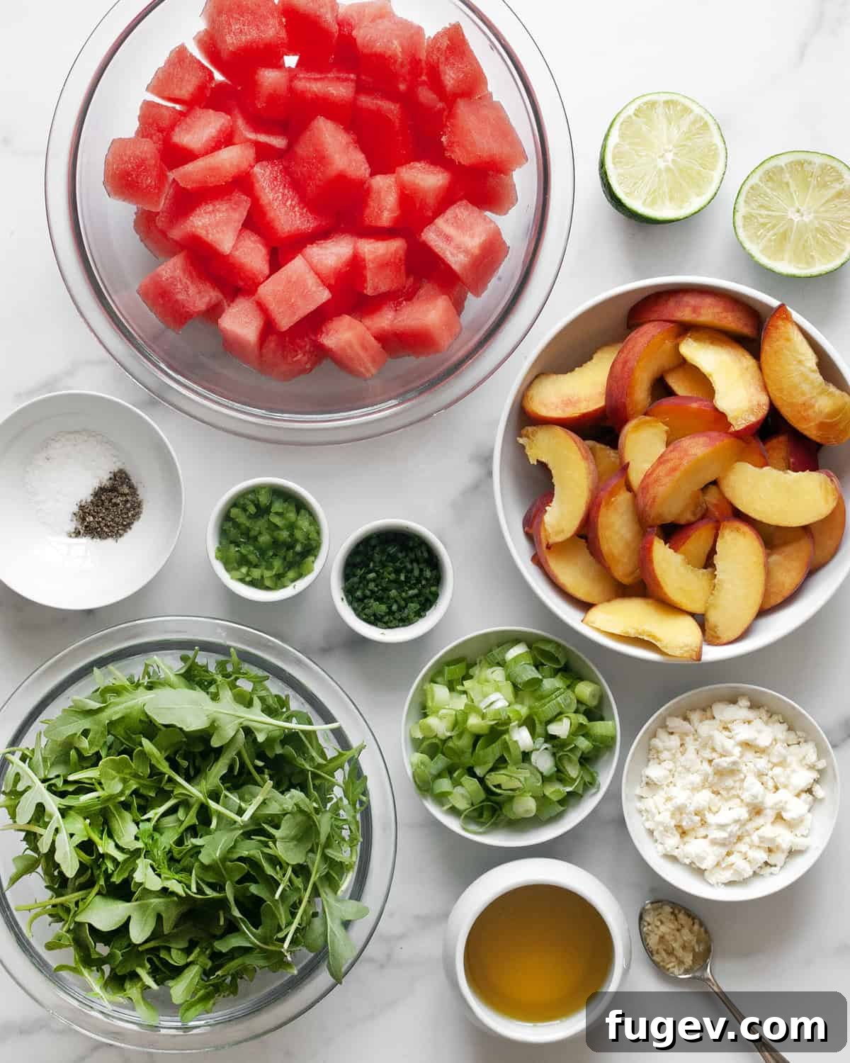 Watermelon Peach Bliss 3 A flat lay of fresh ingredients for watermelon peach salad, including watermelon cubes, peach slices, a bunch of arugula, scallions, feta cheese, chives, a lime, a jalapeno, and olive oil.