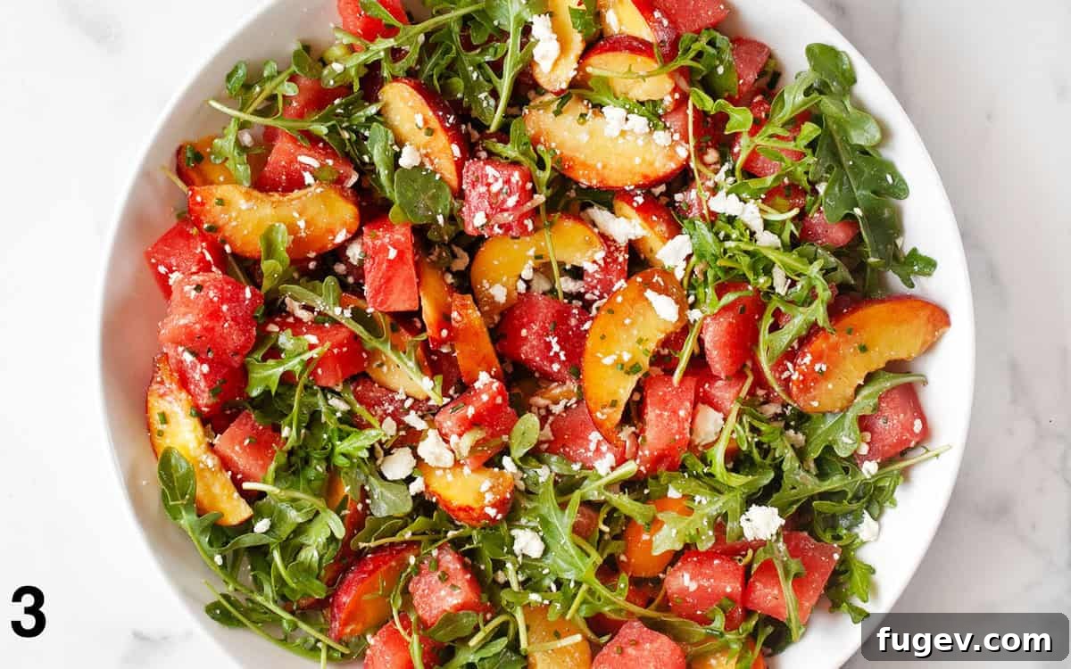 Watermelon Peach Bliss 5 A large bowl of watermelon peach salad, now fully tossed with dressing and arugula, showcasing the vibrant ingredients.