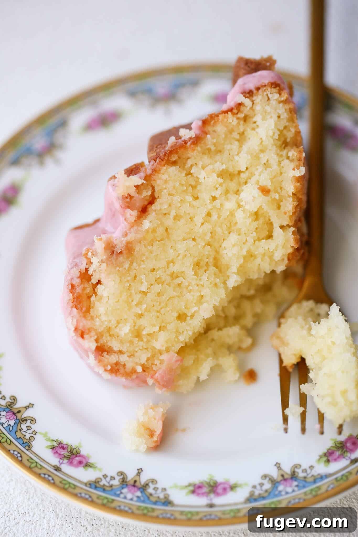 Zesty Lemon Loaf 3 A slice of Lemon Pound Cake with strawberry icing, elegantly placed on a delicate china plate with a gold fork, ready to be enjoyed.