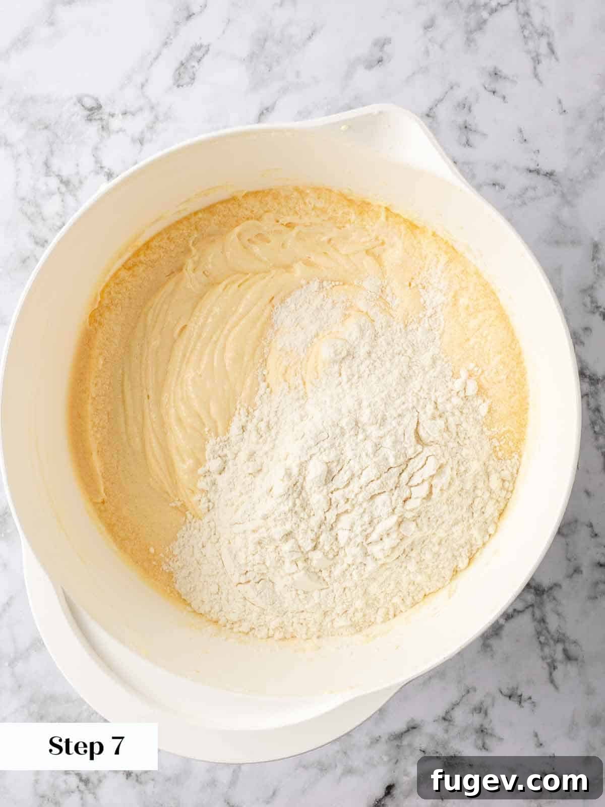 Zesty Lemon Loaf 7 Mixing the dry ingredients into the lemon pound cake batter, ensuring no lumps remain for a smooth consistency.
