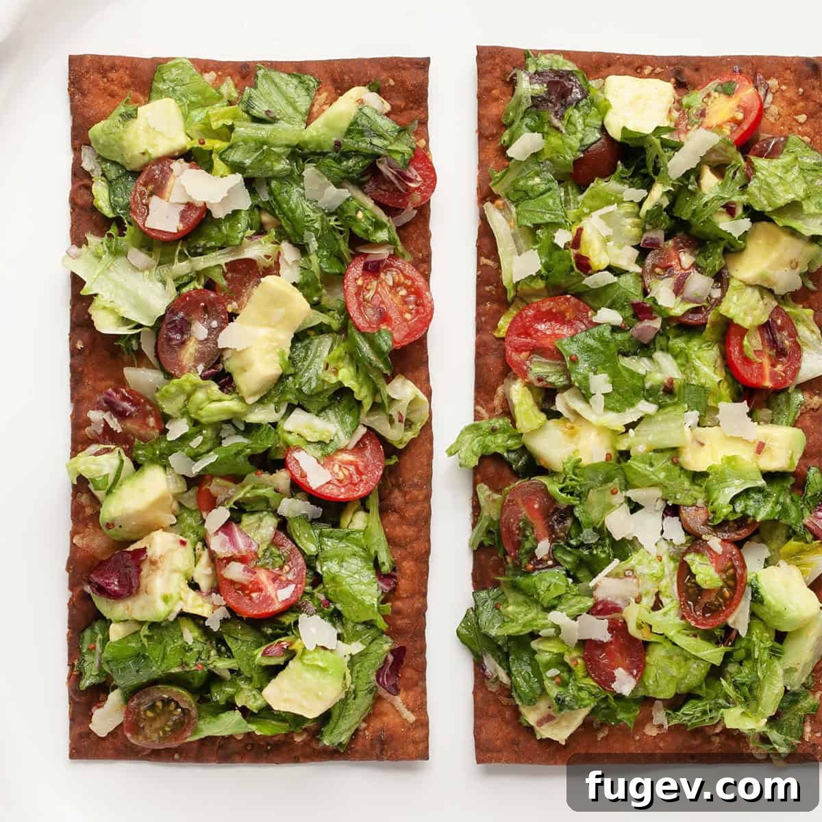 Crispy Lavash Garden Flatbread 2 Two rectangular lavash bread pizzas generously topped with vibrant mixed greens, cherry tomatoes, avocado, and shaved Parmesan. They are ready to be served on a rustic wooden surface.