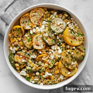 Grilled zucchini, yellow squash and corn in bowl, garnished with feta and herbs.
