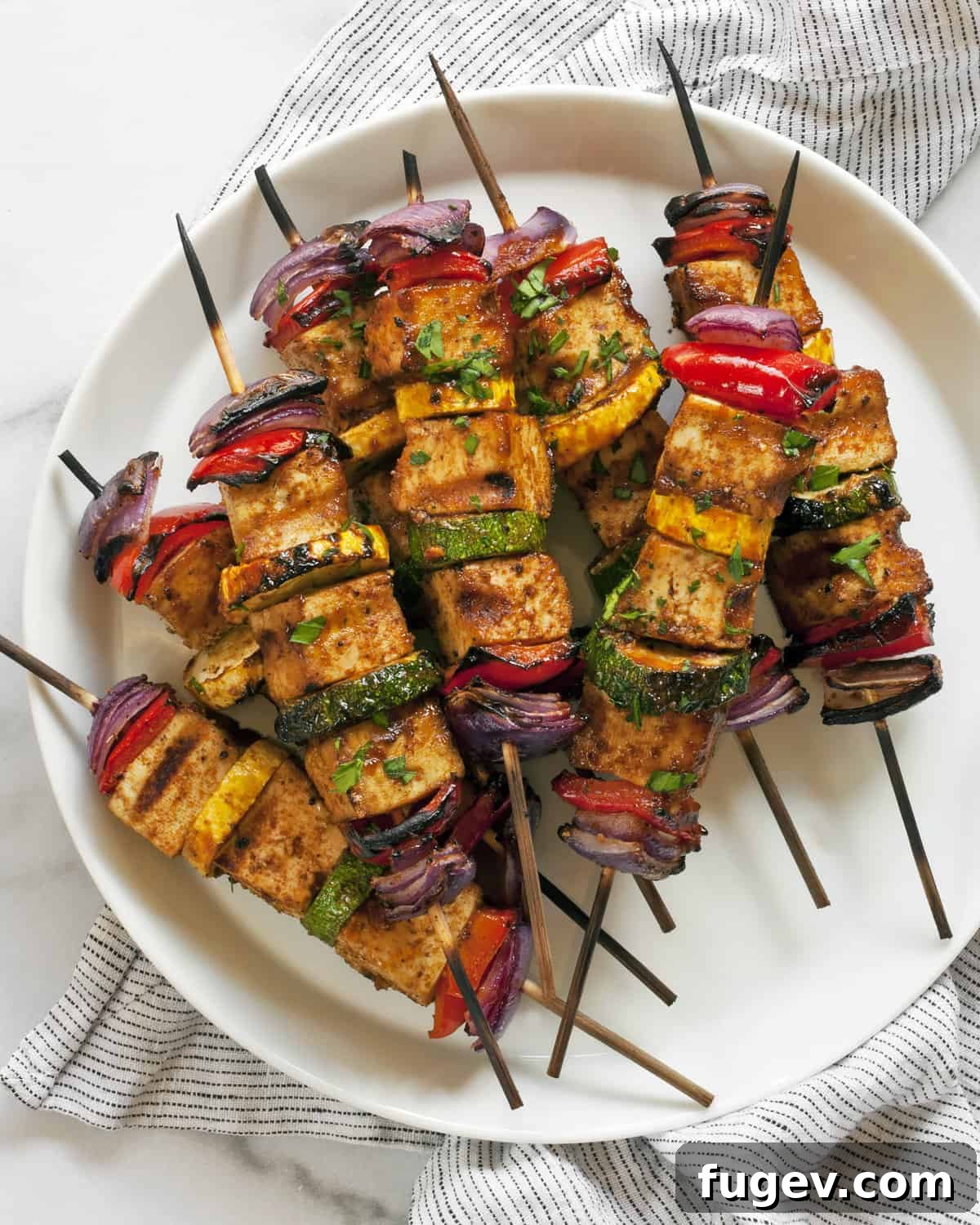 Smoky Tofu and Vibrant Veggie Skewers 2 Stacked BBQ tofu veggie skewers on a plate, showcasing grilled tofu, zucchini, yellow squash, bell peppers, and red onions with a barbecue glaze.