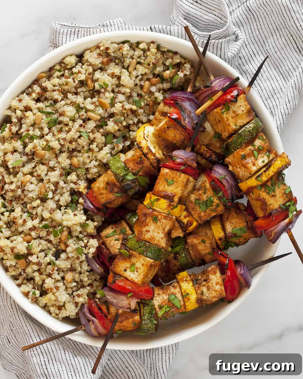 Smoky Tofu and Vibrant Veggie Skewers 6 BBQ tofu veggie skewers served in a bowl with herby lemon quinoa, garnished with fresh herbs.