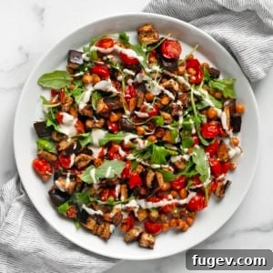 Roasted eggplant, tomatoes and chickpeas drizzled with lemon tahini sauce on a plate.