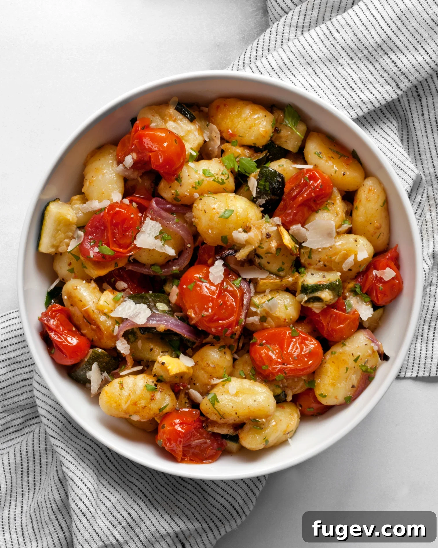 Sheet Pan Gnocchi Harvest 6 A close-up shot of sheet pan gnocchi with roasted vegetables in a serving bowl, garnished with fresh herbs and Parmesan.