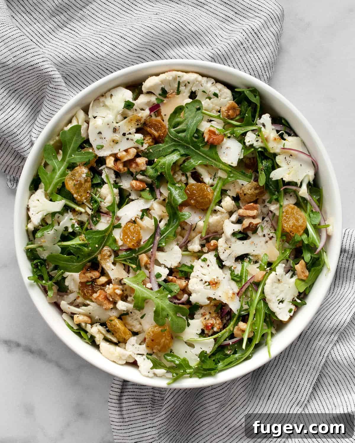 Crisp Cauliflower Salad with Walnuts and Tangy Pickled Raisins 2 Salad with sliced cauliflower and arugula in a bowl.