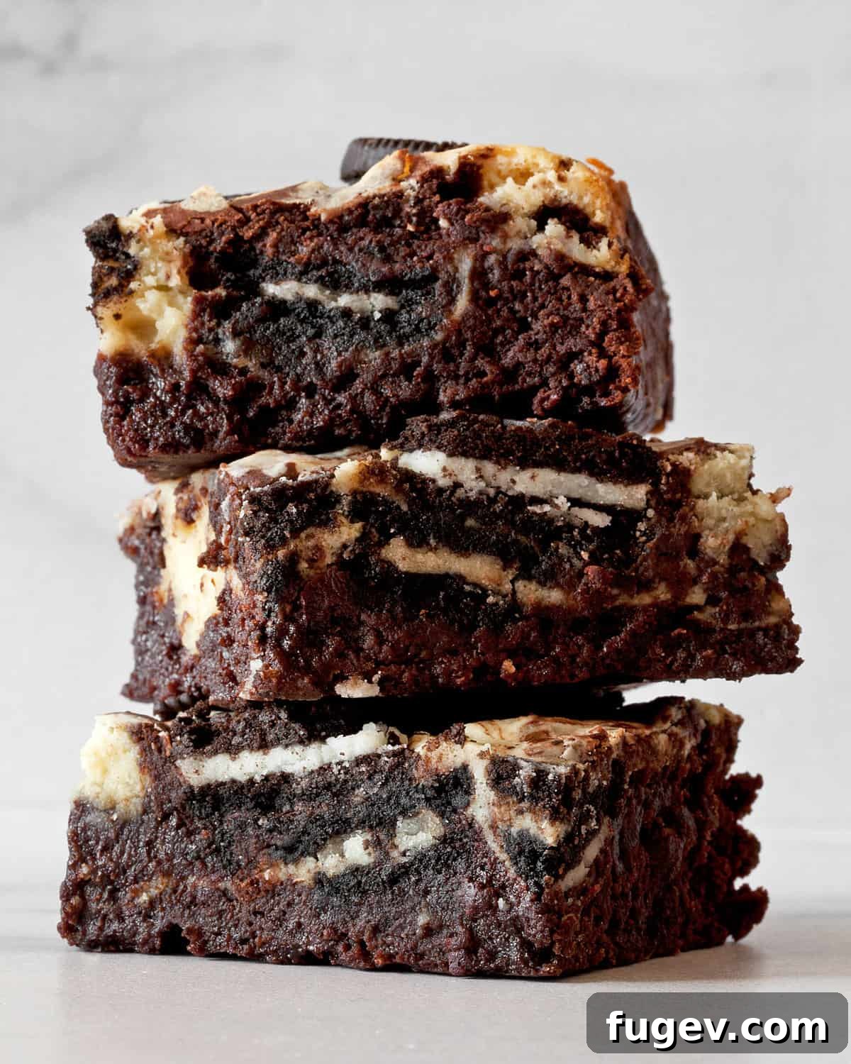 Swirled Cream Cheese Brownies 2 A stack of three incredibly fudgy cream cheese brownies, showcasing the rich chocolate, creamy cheesecake swirl, and scattered Oreo cookie pieces.