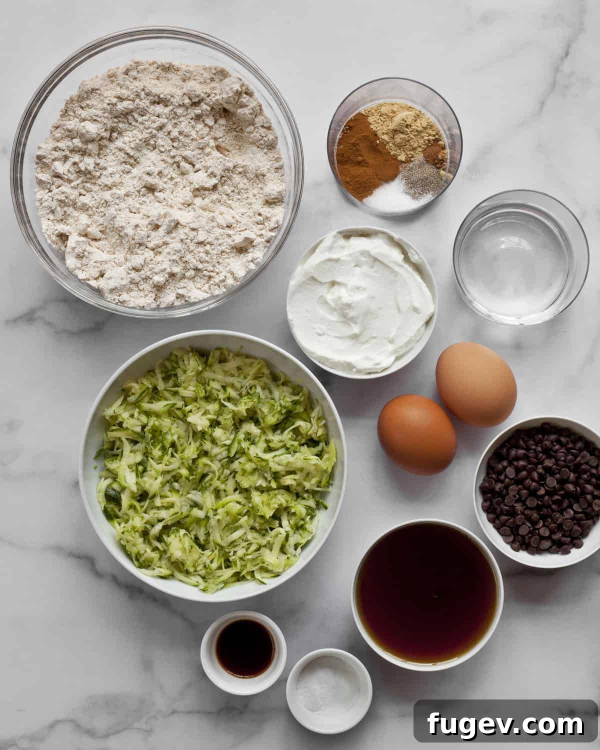 Wholesome Chocolate Chip Zucchini Delights 3 A selection of fresh ingredients laid out, including whole wheat pastry flour, shredded zucchini, eggs, vanilla extract, Greek yogurt, and a vibrant array of aromatic spices.