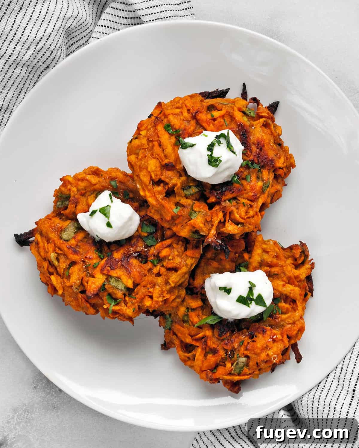Golden Sweet Potato Fritter Bites 2 Three golden-brown sweet potato fritters, elegantly topped with a dollop of creamy Greek yogurt and sprinkled with freshly chopped parsley, arranged on a rustic plate.
