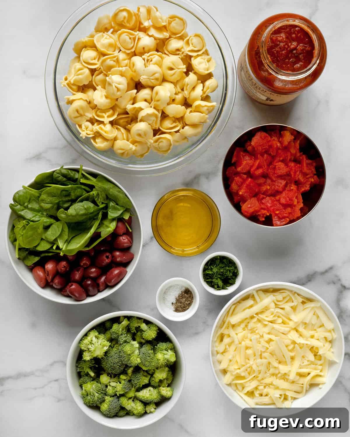 Mediterranean Tortellini Bake 3 A vibrant display of ingredients including fresh tortellini, olives, spinach, diced tomatoes, shredded cheese, olive oil, and raw broccoli florets.
