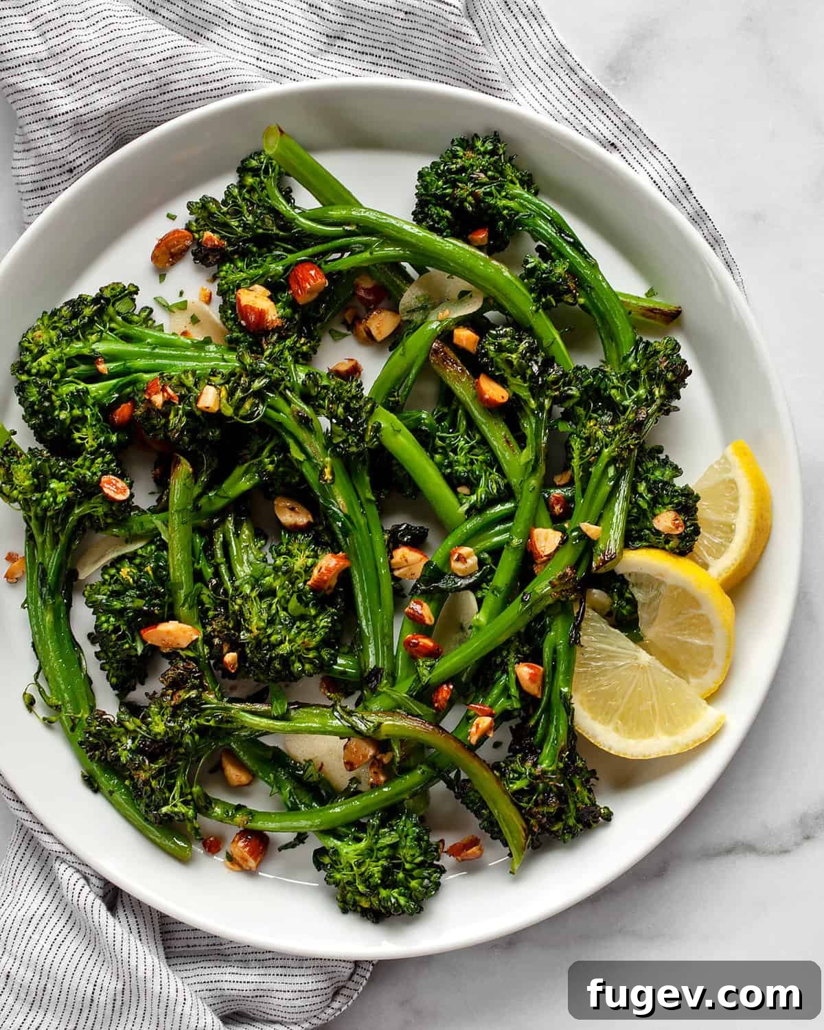 Toasted Almond Broccolini Sauté 2 Perfectly sautéed broccolini piled high on a white plate, garnished with vibrant green parsley and golden spiced almonds, with fresh lemon wedges on the side, ready to be served.