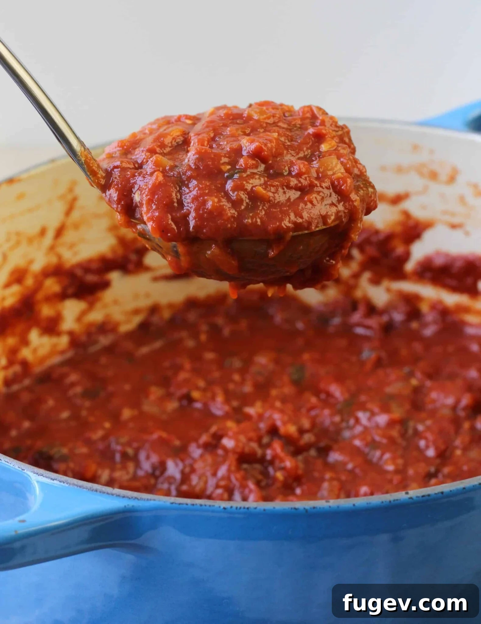Robust Red Wine Pasta Sauce 2 Red Wine Basil Pasta Sauce in a light blue dutch oven with a ladle full of sauce.