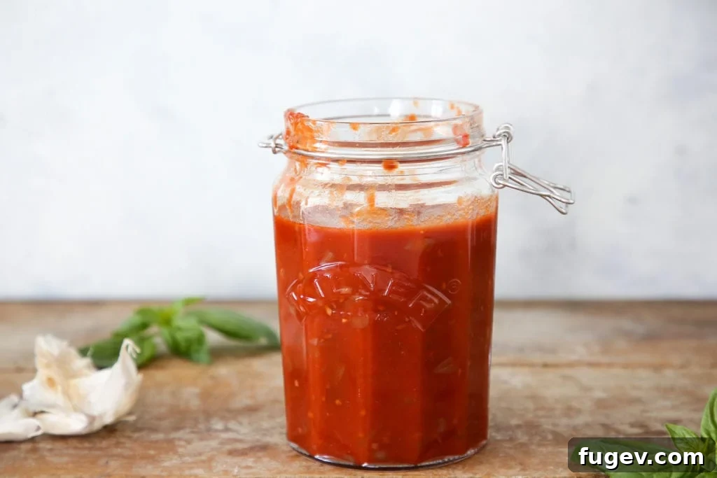 Robust Red Wine Pasta Sauce 4 Red wine pasta sauce inside a clear jar on a wood surface with fresh garlic and herbs.