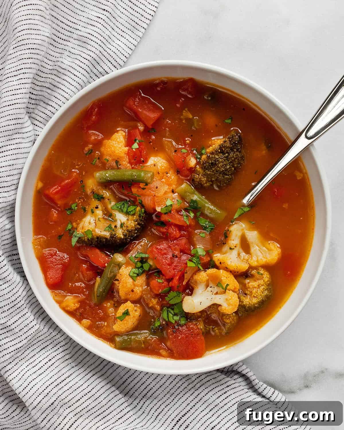Comforting Harvest Vegetable Soup 2 A steaming bowl of hearty vegetable soup, rich with large pieces of broccoli, green beans, and cauliflower, garnished with fresh herbs, ready to be enjoyed.
