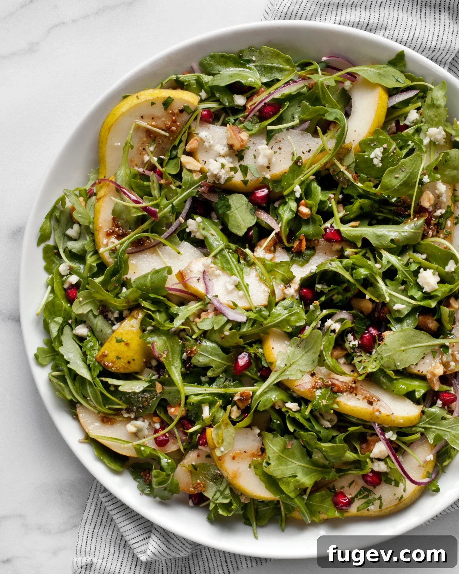 Juicy Pear and Creamy Gorgonzola Salad 2 A beautifully arranged Pear Gorgonzola Salad on a white plate, showcasing vibrant arugula, sliced pears, crumbled blue cheese, and red pomegranate seeds.