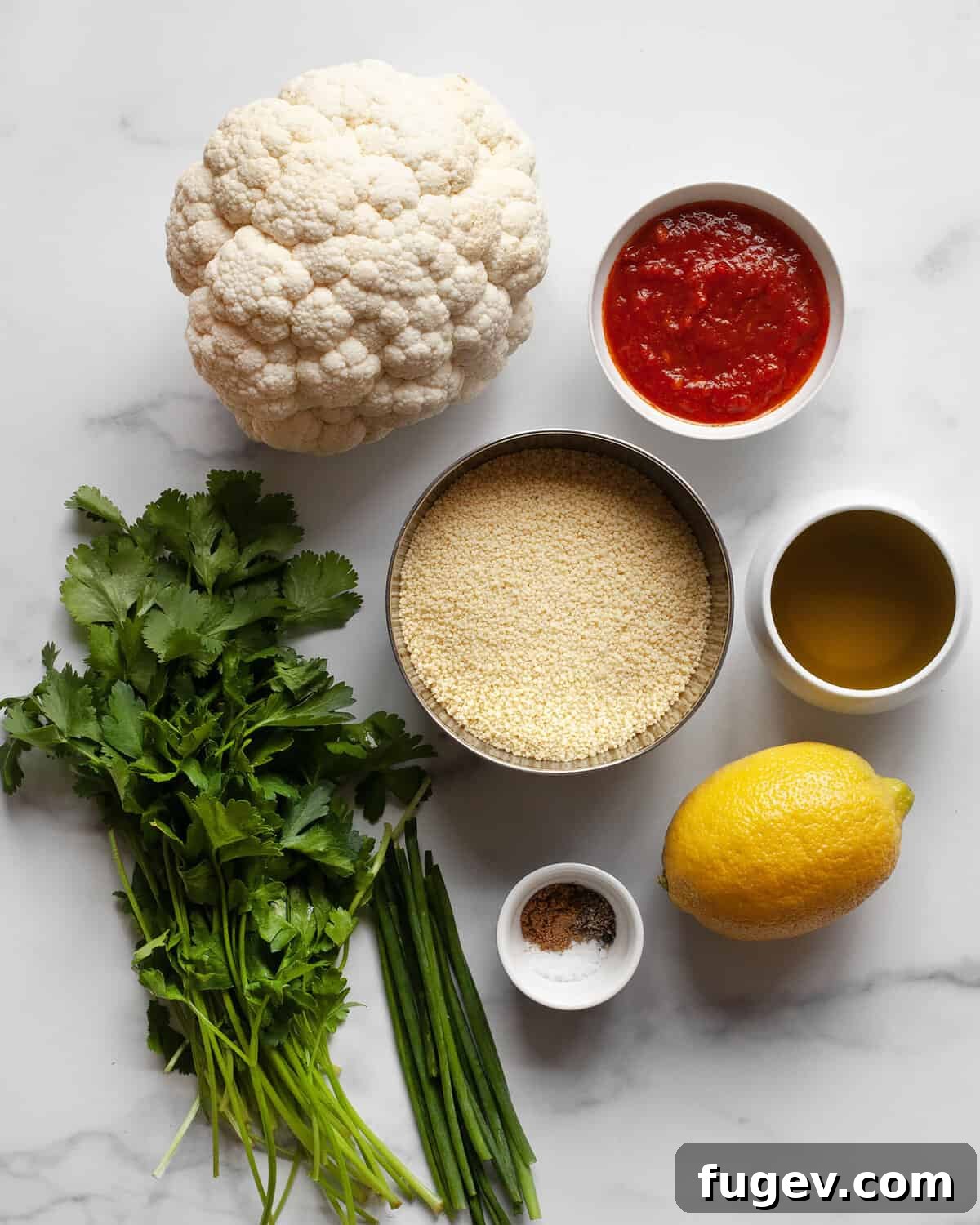 Zesty Harissa Roasted Cauliflower Couscous 3 A flat lay of all the fresh ingredients needed for Harissa Roasted Cauliflower Couscous, including a head of cauliflower, couscous, fresh herbs, spices, harissa paste, and olive oil.