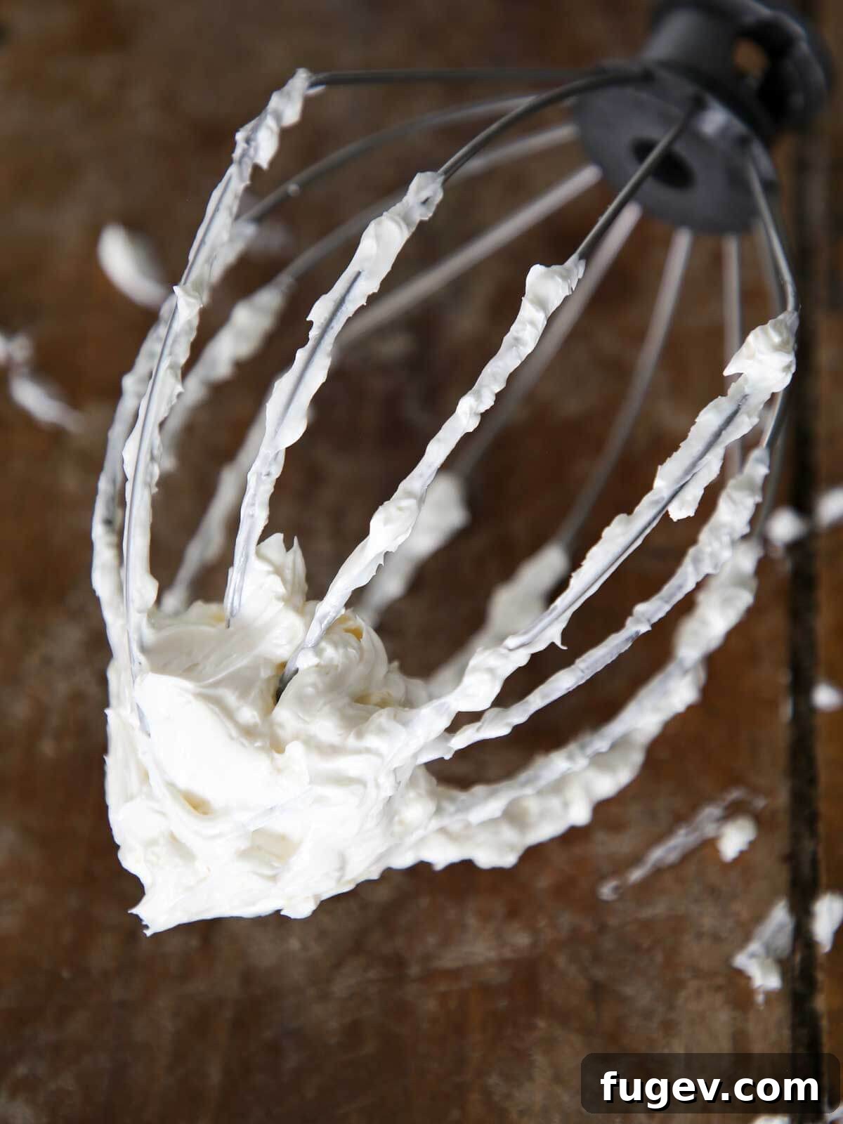 Dreamy Swiss Meringue Buttercream 2 Silky smooth Swiss Meringue Buttercream on a whisk, resting on a rustic wooden surface.