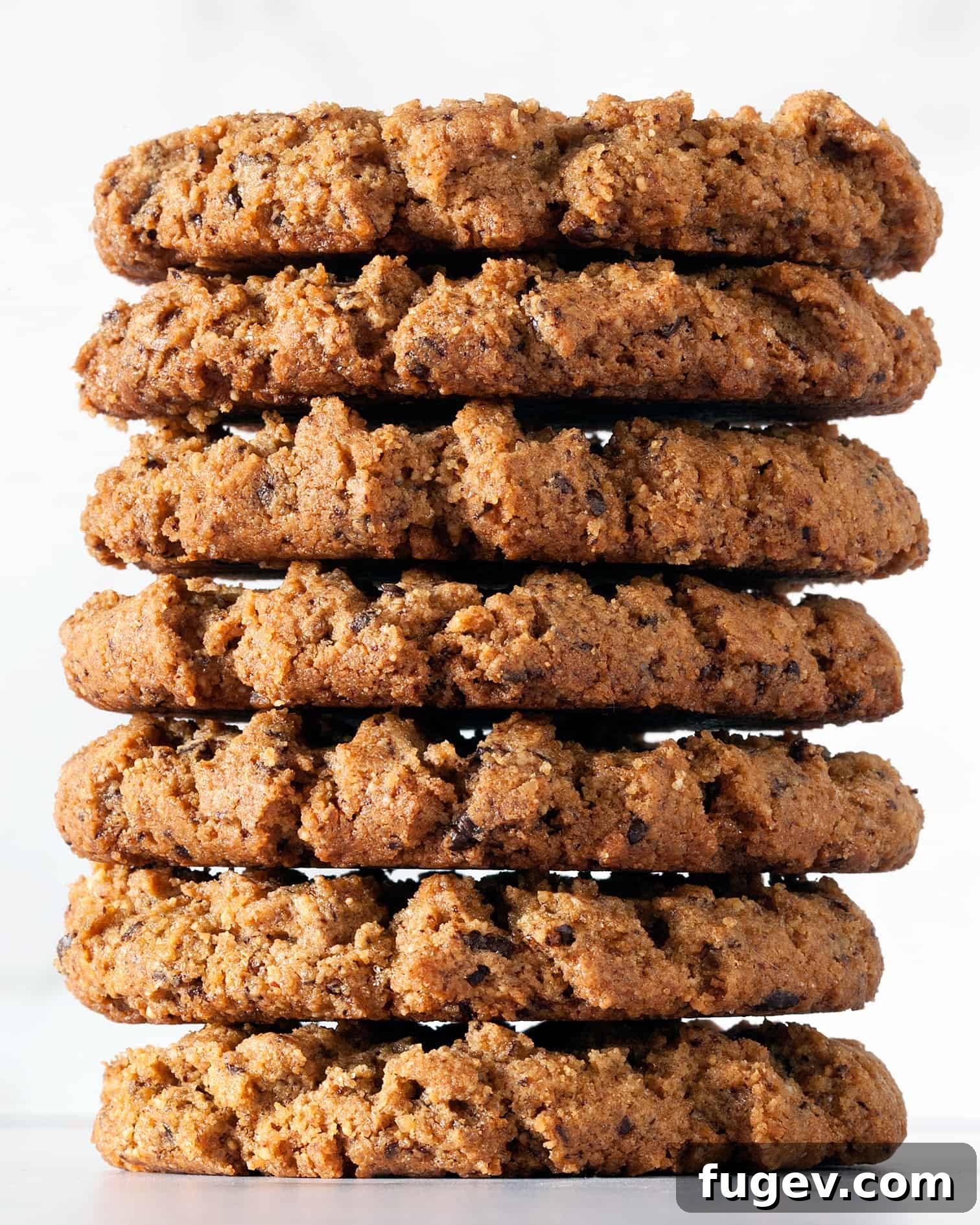Decadent Peanut Butter Chocolate Chews 3 A stack of golden-brown flourless peanut butter cookies with visible chocolate flecks, presented appealingly on a cooling rack.