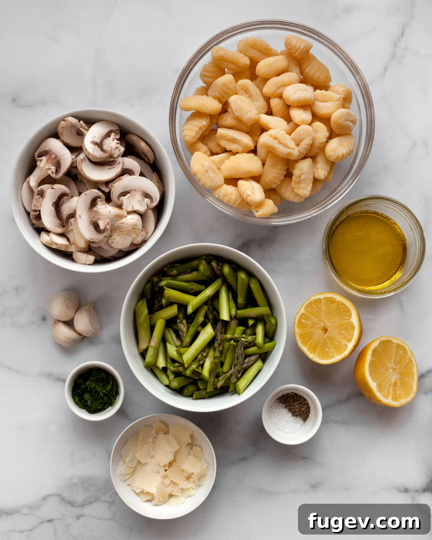 Garden Gnocchi Sheet Pan Feast 3 A flat lay photograph of all the ingredients needed for Sheet Pan Asparagus Mushroom Gnocchi, including a package of gnocchi, sliced mushrooms, trimmed asparagus, a whole lemon, fresh garlic cloves, a bottle of olive oil, a wedge of Parmesan cheese, and fresh parsley.