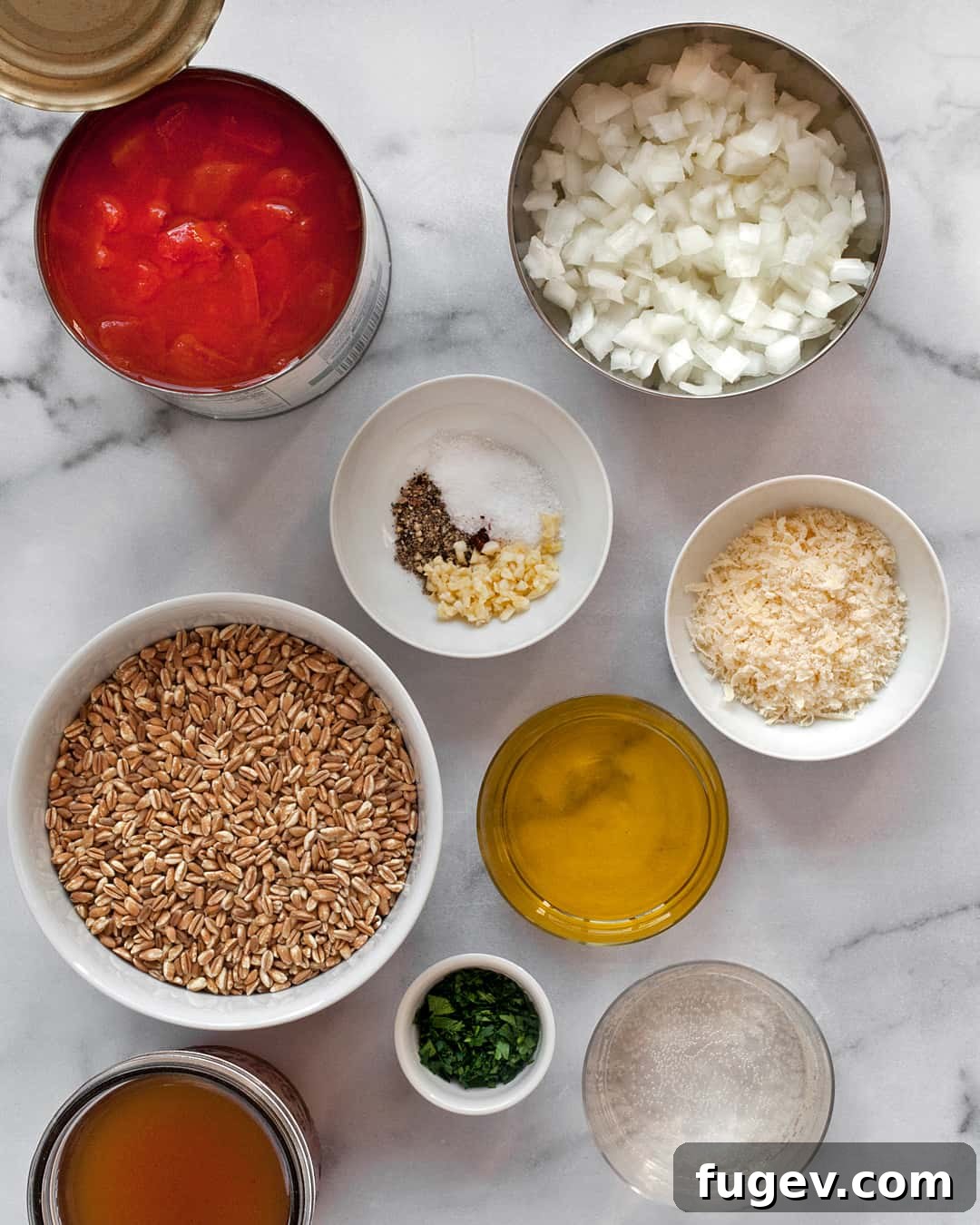 Hearty Tomato Farro Bake 3 A flat lay photograph of all the raw ingredients needed for baked tomato farro risotto, including farro, canned diced tomatoes, fresh onions, garlic cloves, a selection of spices, and vegetable broth.