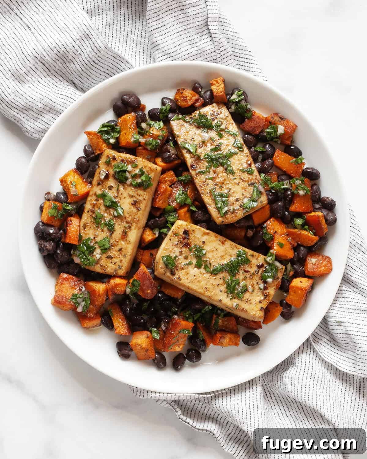 Hearty Sheet Pan Tofu Sweet Potato Black Bean Dinner 2 A beautifully plated serving of sheet pan tofu, sweet potato, and black beans, drizzled generously with green chimichurri sauce.