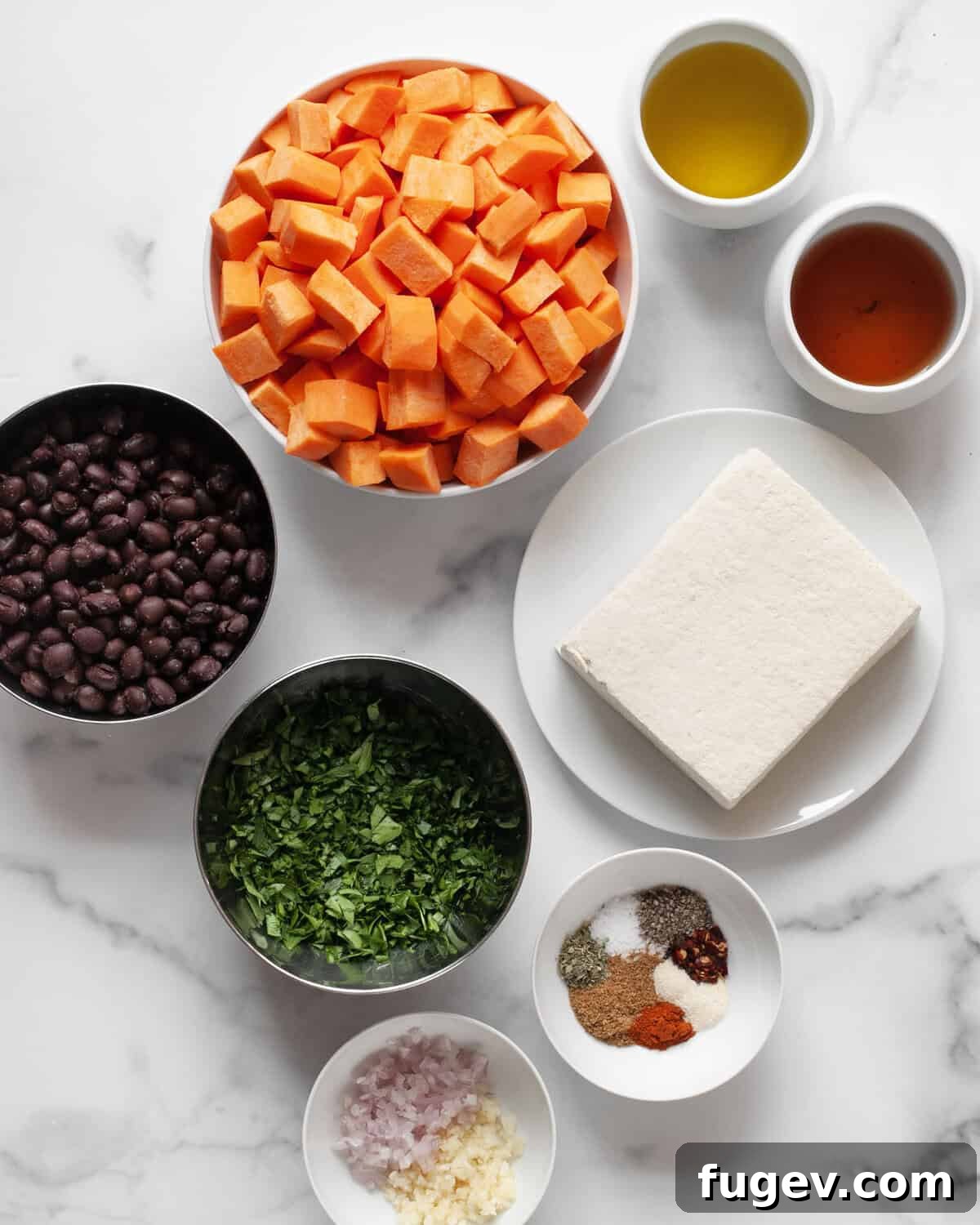 Hearty Sheet Pan Tofu Sweet Potato Black Bean Dinner 3 Arrangement of fresh ingredients including a block of tofu, sweet potatoes, canned black beans, fresh parsley, olive oil, garlic, shallots, red wine vinegar, and various dried spices.