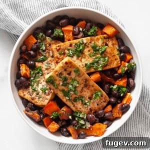 Roasted tofu, sweet potato and black beans in a bowl, garnished with fresh herbs.