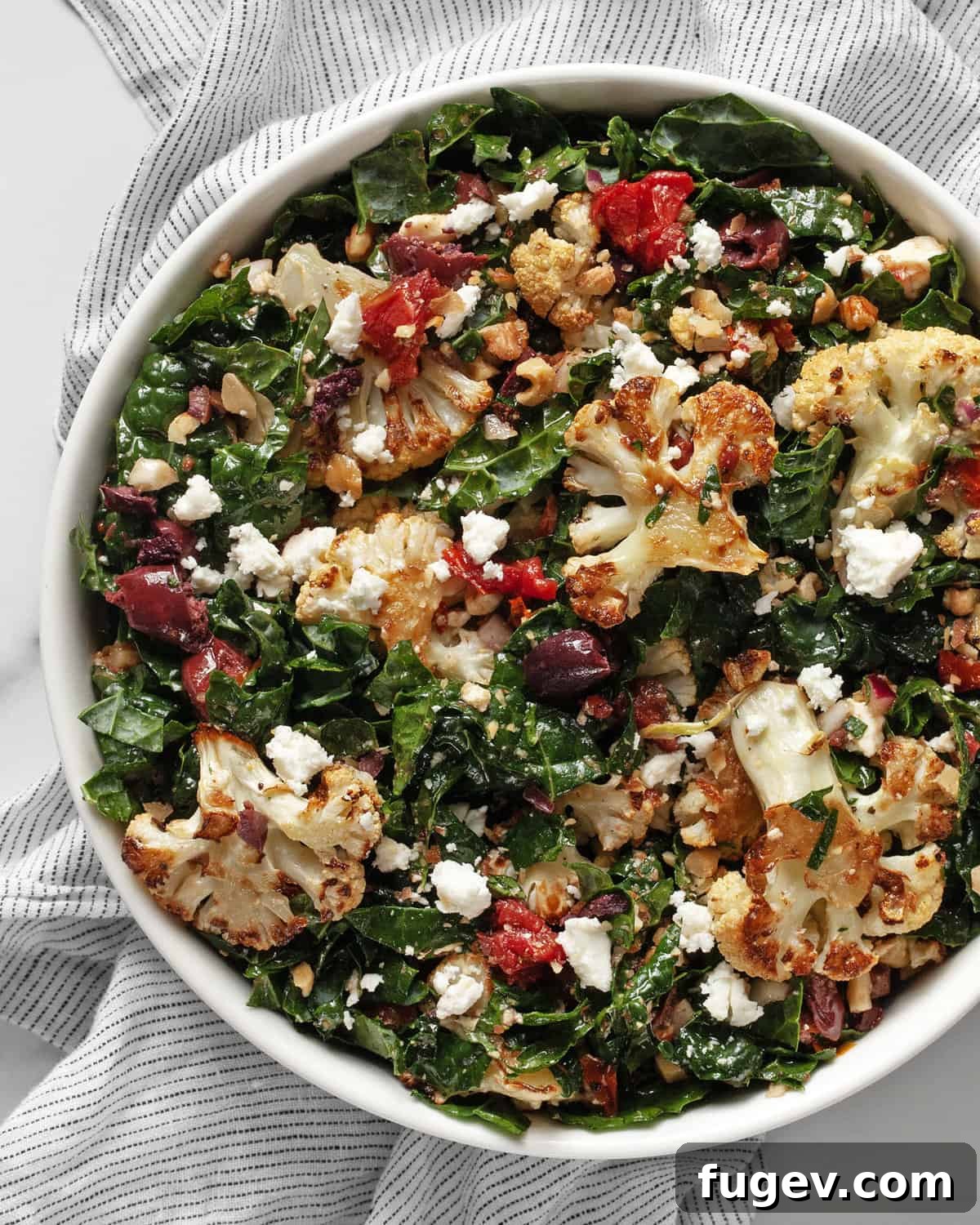 Caramelized Cauliflower Salad 2 A large bowl filled with vibrant roasted cauliflower and kale salad, garnished with sun-dried tomatoes and Kalamata olives.