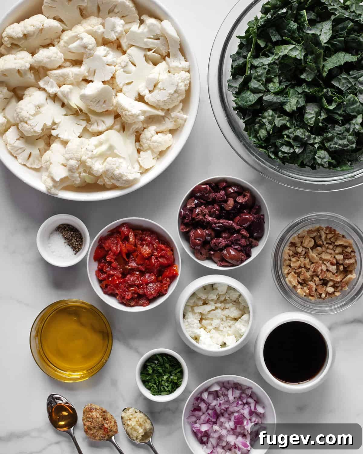 Caramelized Cauliflower Salad 3 A spread of fresh ingredients for the roasted cauliflower kale salad, including whole cauliflower, kale, sun-dried tomatoes, olives, feta, walnuts, red onion, and parsley, along with balsamic vinegar, olive oil, and mustard for the dressing.