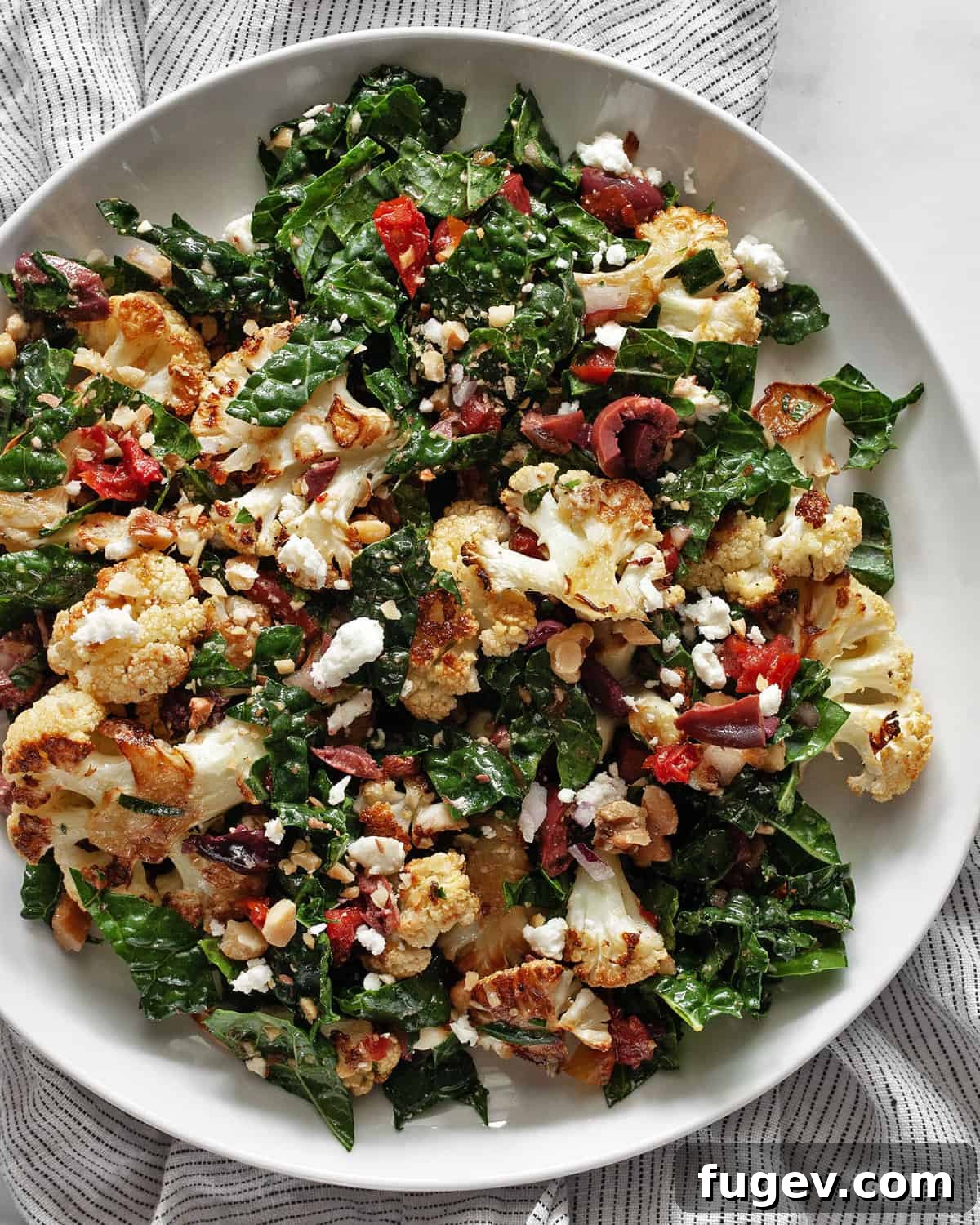 Caramelized Cauliflower Salad 7 A serving of roasted cauliflower and kale salad with sun-dried tomatoes and olives on a white plate, ready to eat.