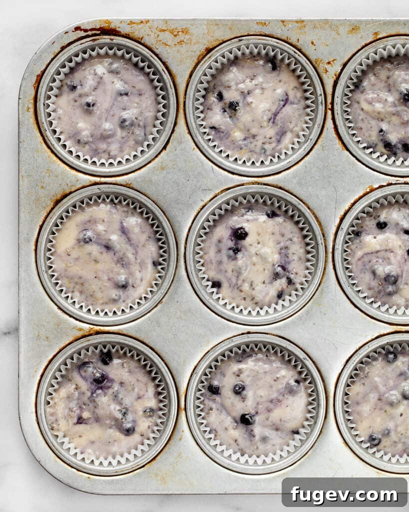 Plant-Based Blueberry Chia Burst Muffins 4 Blueberry muffin batter being spooned into a muffin pan, ready for baking
