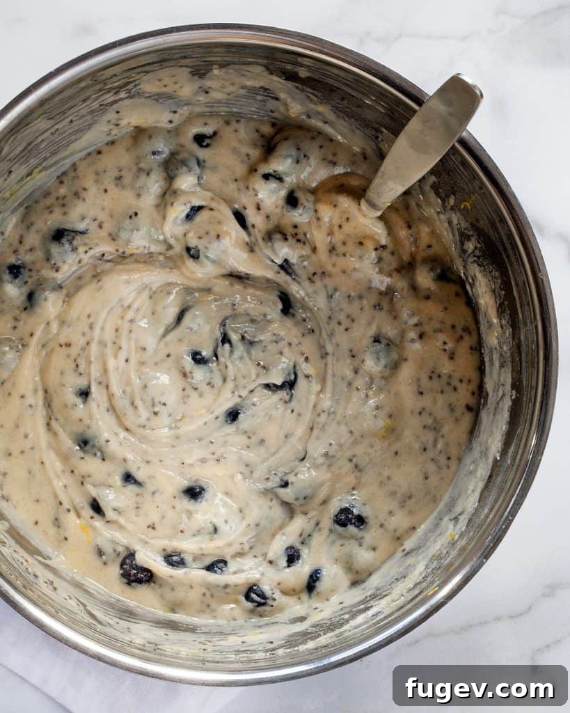 Plant-Based Blueberry Chia Burst Muffins 7 Close-up of muffin batter being stirred in a bowl with blueberries and chia seeds
