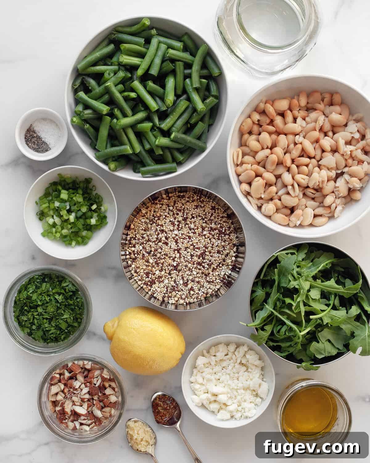 Green Bean Quinoa Bowl with White Beans and Toasted Almonds 3 A flat lay of fresh ingredients including vibrant green beans, creamy white beans, fluffy quinoa, bright lemon, crunchy almonds, crumbled feta, golden olive oil, peppery arugula, aromatic scallions, and seasoning like salt and pepper, ready for preparation.