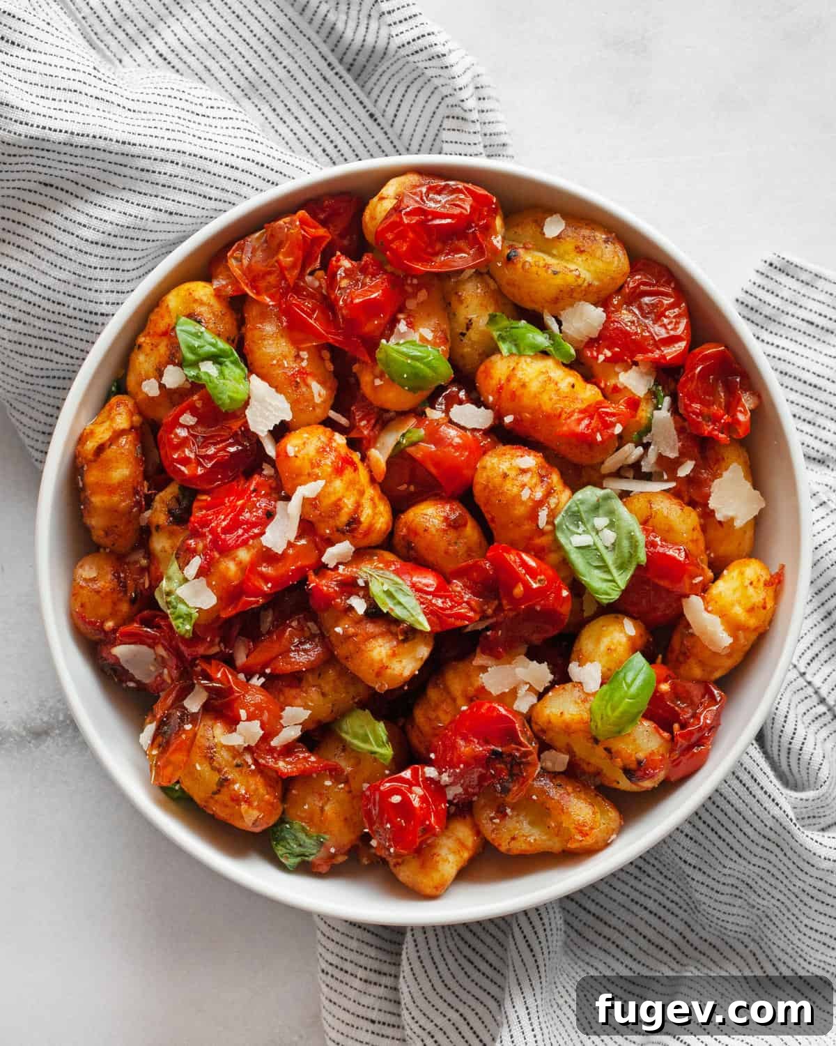 Crispy Gnocchi with Burst Cherry Tomatoes 2 A vibrant bowl of roasted cherry tomato sheet pan gnocchi, garnished with fresh basil and Parmesan cheese, showcasing a quick and easy vegetarian dinner.