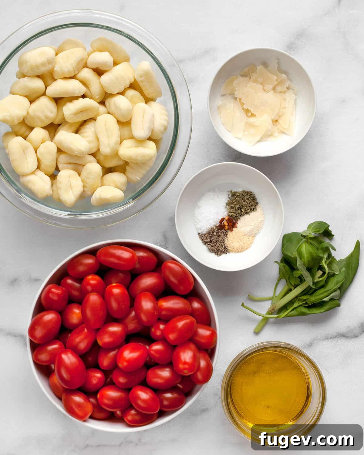Crispy Gnocchi with Burst Cherry Tomatoes 3 A flat lay of fresh ingredients for sheet pan gnocchi: packaged gnocchi, vibrant cherry tomatoes, a selection of dried spices, Parmesan cheese, fresh basil, and a bottle of olive oil.