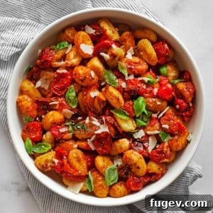 A vibrant bowl of roasted cherry tomato sheet pan gnocchi, garnished with fresh basil and Parmesan cheese.