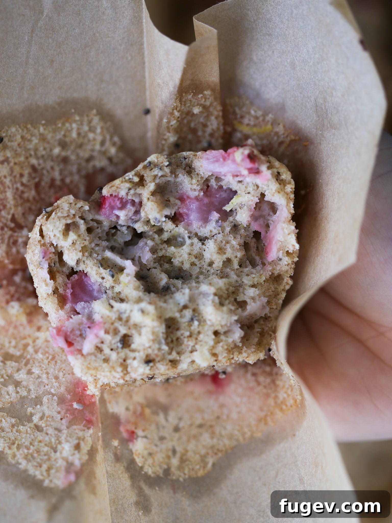 Homemade Strawberry Muffins 12 A hand holding an unwrapped Whole Wheat Strawberry Muffin, showing its inviting texture and the fresh strawberries baked within.