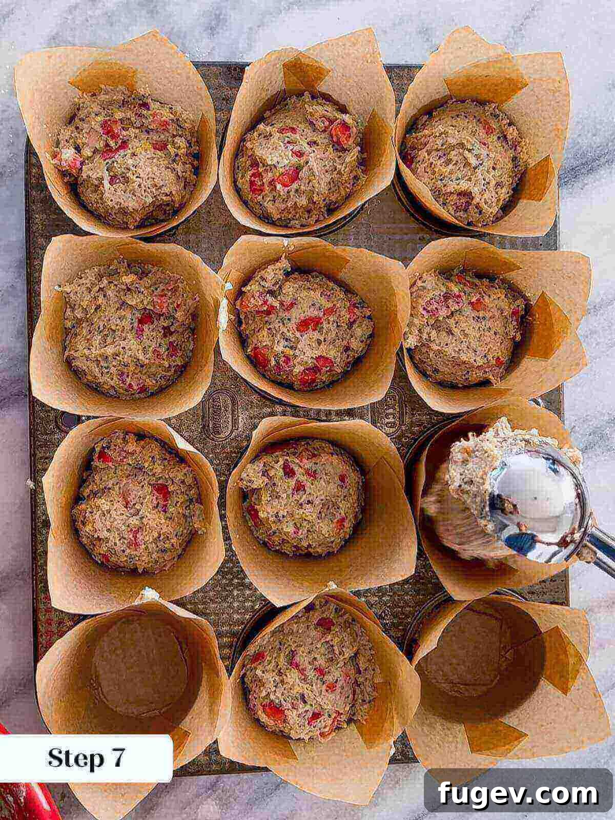 Homemade Strawberry Muffins 10 A large scoop of strawberry muffin batter being carefully portioned into individual muffin cups lined with tulip paper liners.