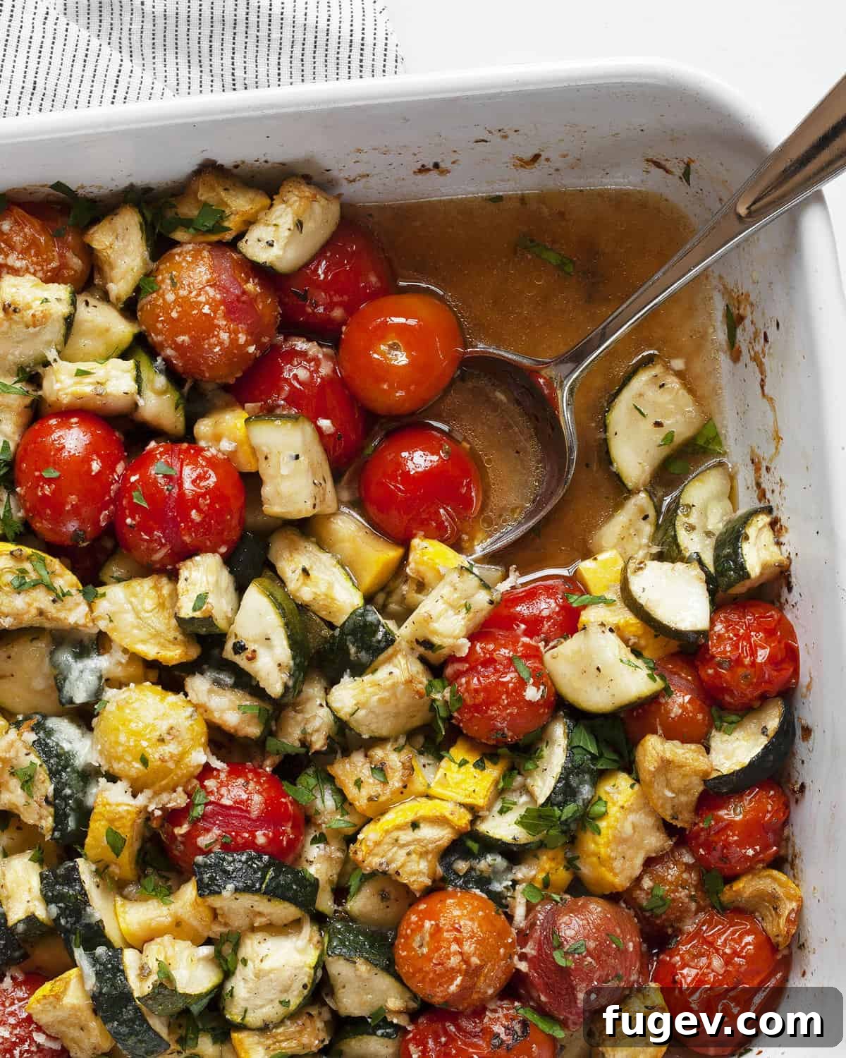 Balsamic Roasted Zucchini and Tomatoes 2 A bubbling zucchini tomato bake fresh out of the oven, with a serving spoon nestled in the casserole dish, highlighting the tender vegetables and melted Parmesan cheese.